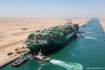 Ever Given container ship stuck diagonally in the Suez Canal with tugboats working to refloat it.